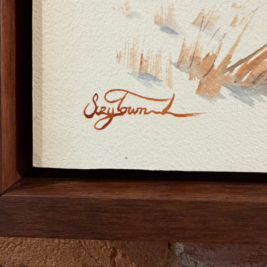 Close-up of a signature on a painting with a wooden frame.