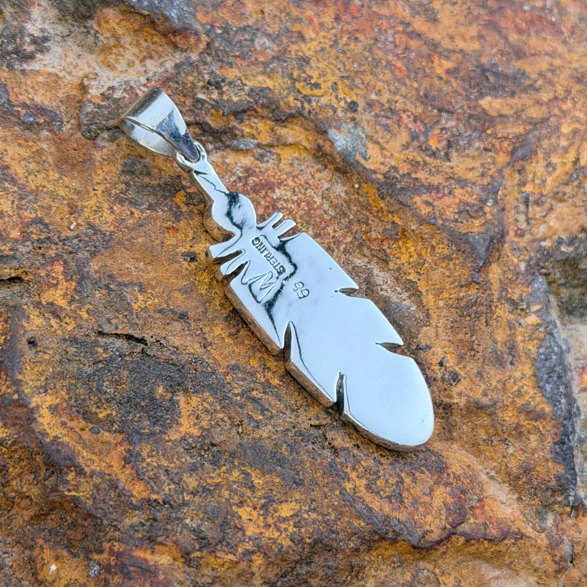 Sterling Silver pendant inlaid with turquoise in the shape of a feather. it rests on a rock.
