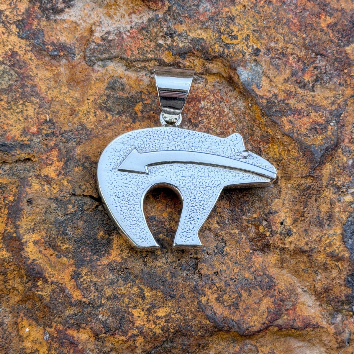 A silver pendant in the shape of a bear with an arrow motiff running along is horizontally