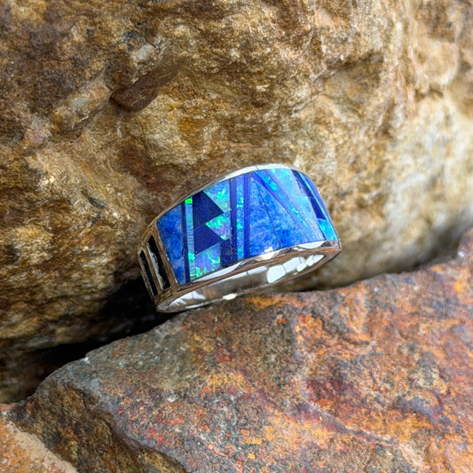 David Rosales Sterling Silver Ring with Inlaid Multicolored blue stones. Its inlay contains dark blue, light blue, and a blue opal. It rests on a rock surface.