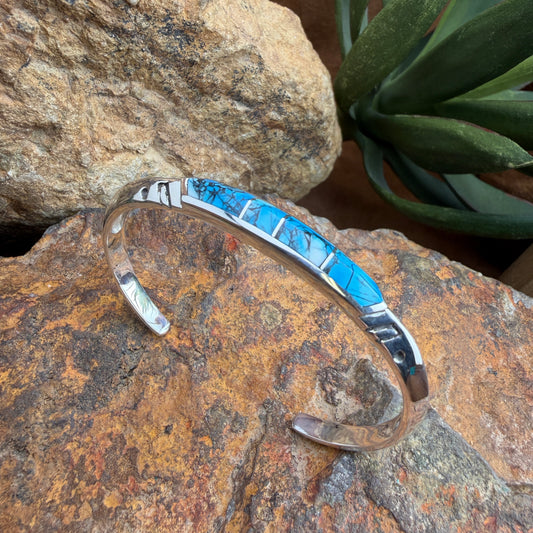 Silver and blue inlay bracelet on a textured stone surface with a plant in the background