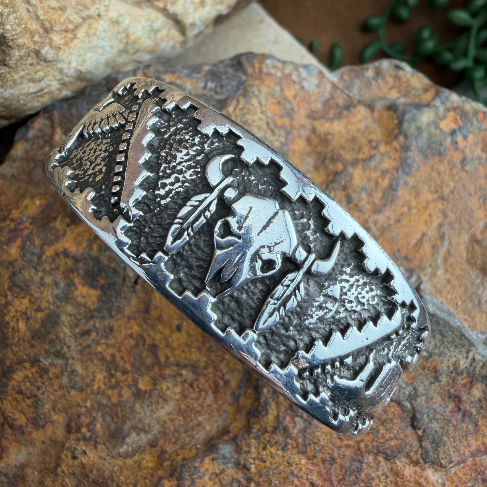 Silver bracelet with intricate designs  of a buffalo skull, landscape, and eagle