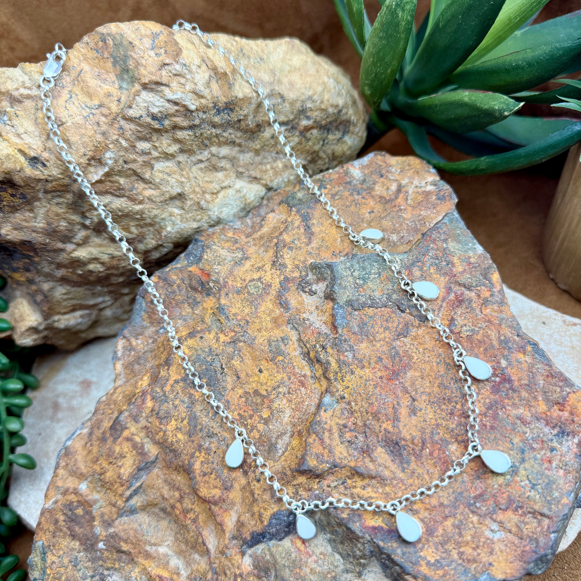 Silver necklace with teardrop pendants on a textured stone surface