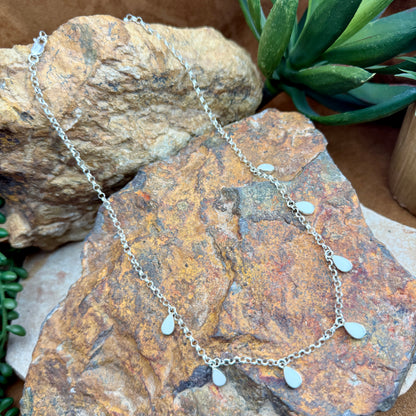 Silver necklace with teardrop pendants on a textured stone surface
