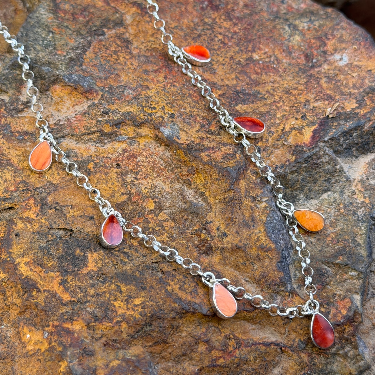 Close up of orange spiny oyster stone that in inlaid in a tear drop form on a sterling silver necklace