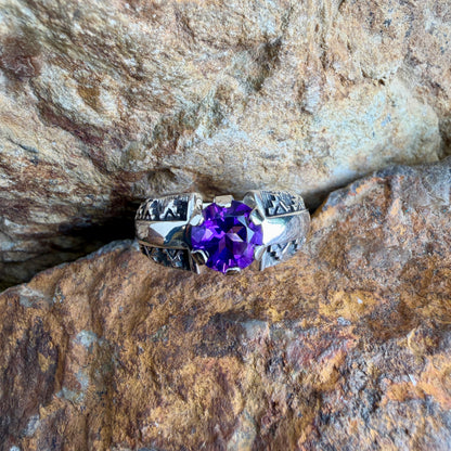 Silver ring with a purple gemstone on a rocky surface