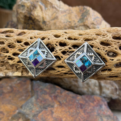 Geometric Sterling Silver studs from the David Rosales collection. A small inlaid diamond  with blue, purple, and opal rests on the inside of a larger diamond that features intricate sand casted geometric pueblo designs. They rest on a piece of driftwood.