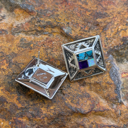 Geometric Sterling Silver studs from the David Rosales collection. A small inlaid diamond  with blue, purple, and opal rests on the inside of a larger diamond that features intricate sand casted geometric pueblo designs. One is flipped over to showcase the post and stamping. They rest on a piece of driftwood.