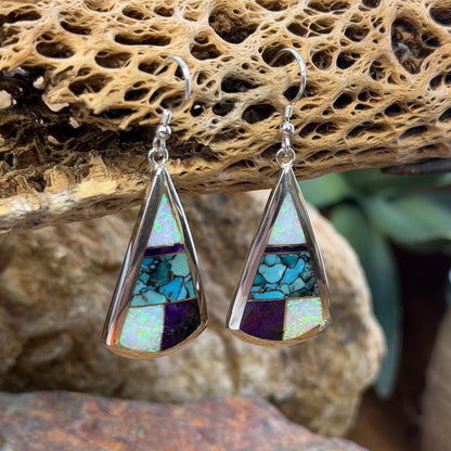 Triangle Drop Earrings inlaid with purple, turquoise and opal. They hang from a piece of driftwood
