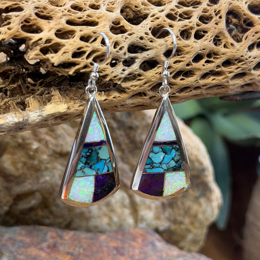 Triangle Drop Earrings inlaid with purple, turquoise and opal. They hang from a piece of driftwood