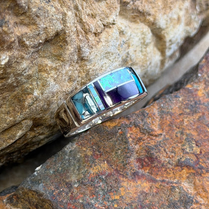 David rosales multicolored inlaid sterling silver ring. It has inlaid purple, turquoise and opal stones. It rests in-between two rocks.