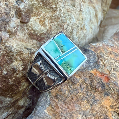 A wide Sterling Silver David Rosales Ring that features inlaid blue-green hues of Sonoran Gold Turquoise accented by raised sterling silver lines. The band features a raised axe Motif. It rests on a rocky surface.