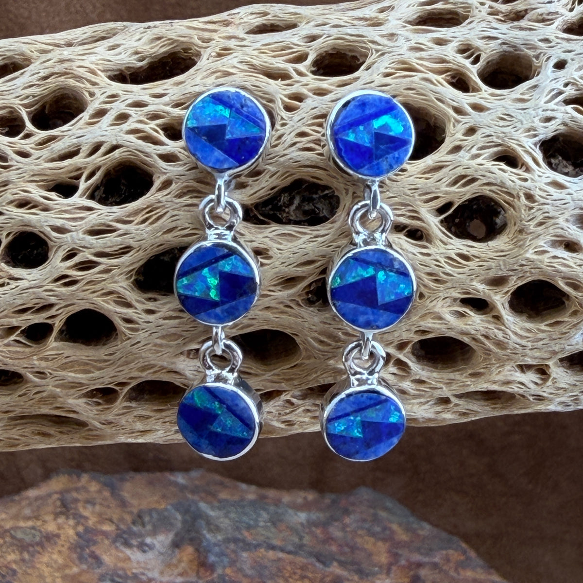 pair of earrings with three small circles inlaid with blue stones hanging from a cactus spine