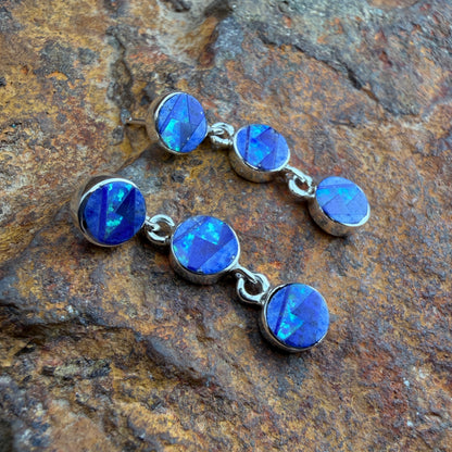 a pair of silver earrings inlaid with blue stones displayed on an orange and brown rock
