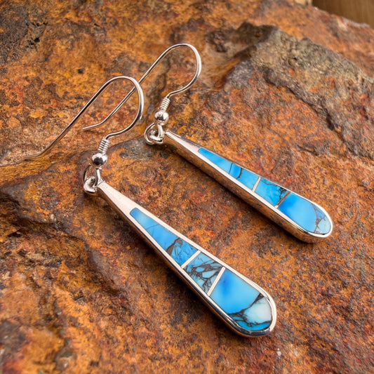 Silver earrings with blue stone inlay on a textured brown surface