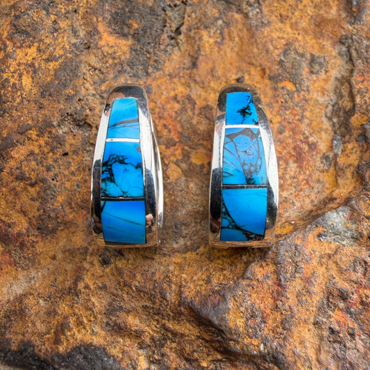 Pair of earrings with dyed dolomite stone inlays on a textured rock surface