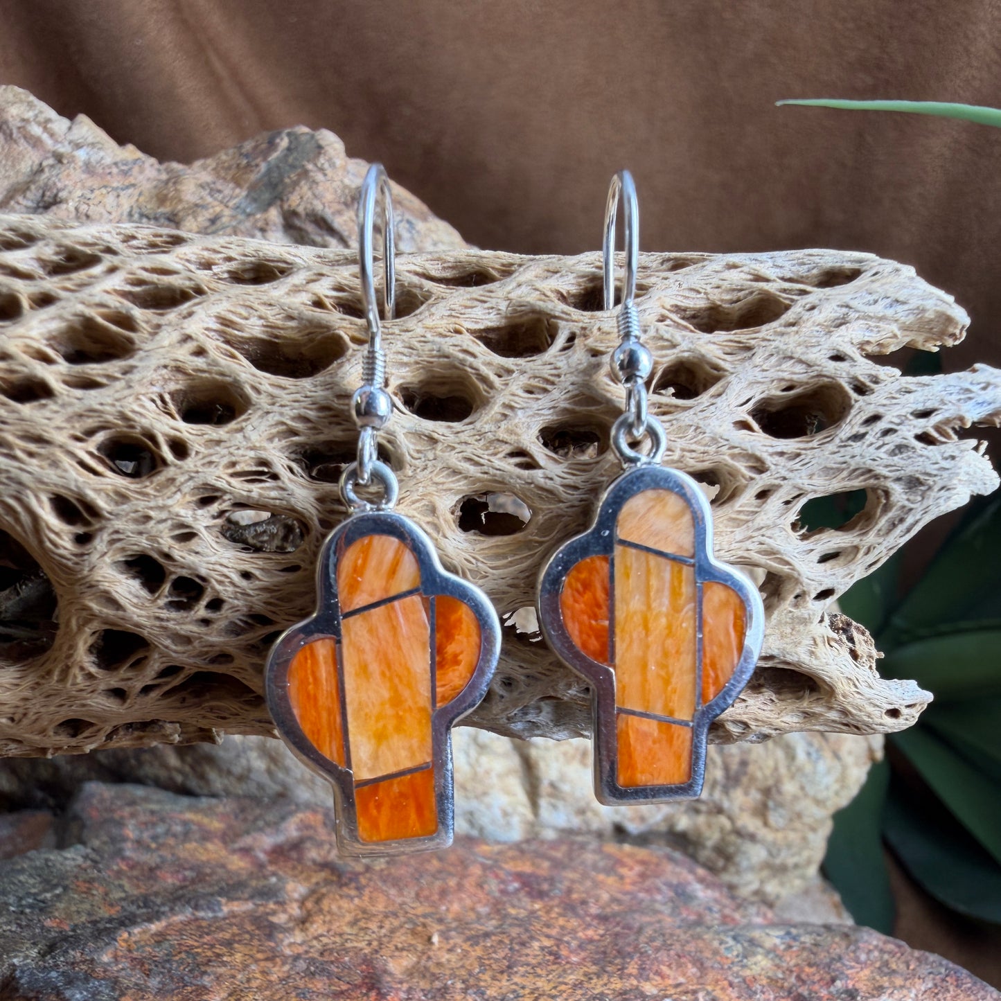 Pair of  cactus earrings with orange and silver design on a textured stone surface
