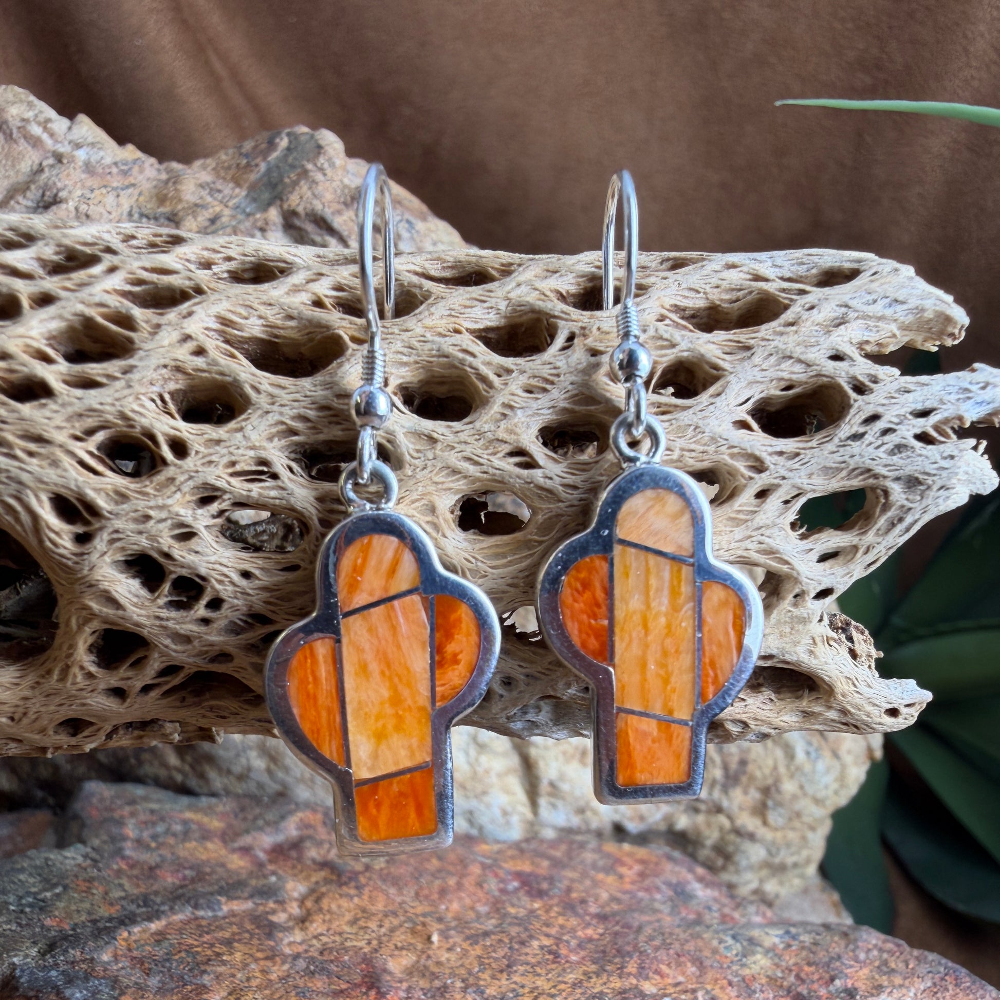 Pair of  cactus earrings with orange and silver design on a textured stone surface