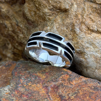 A silver-toned geometric ring with black  details, resting on textured brown and orange rocks.