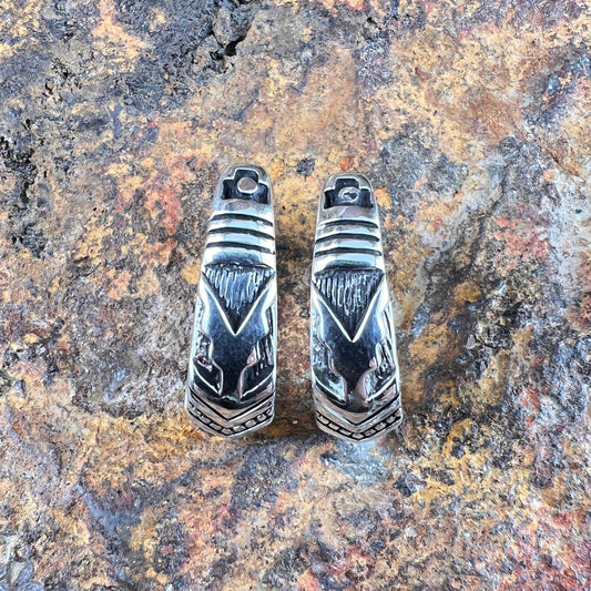 Pair of silver earrings with geometric design on a textured stone surface