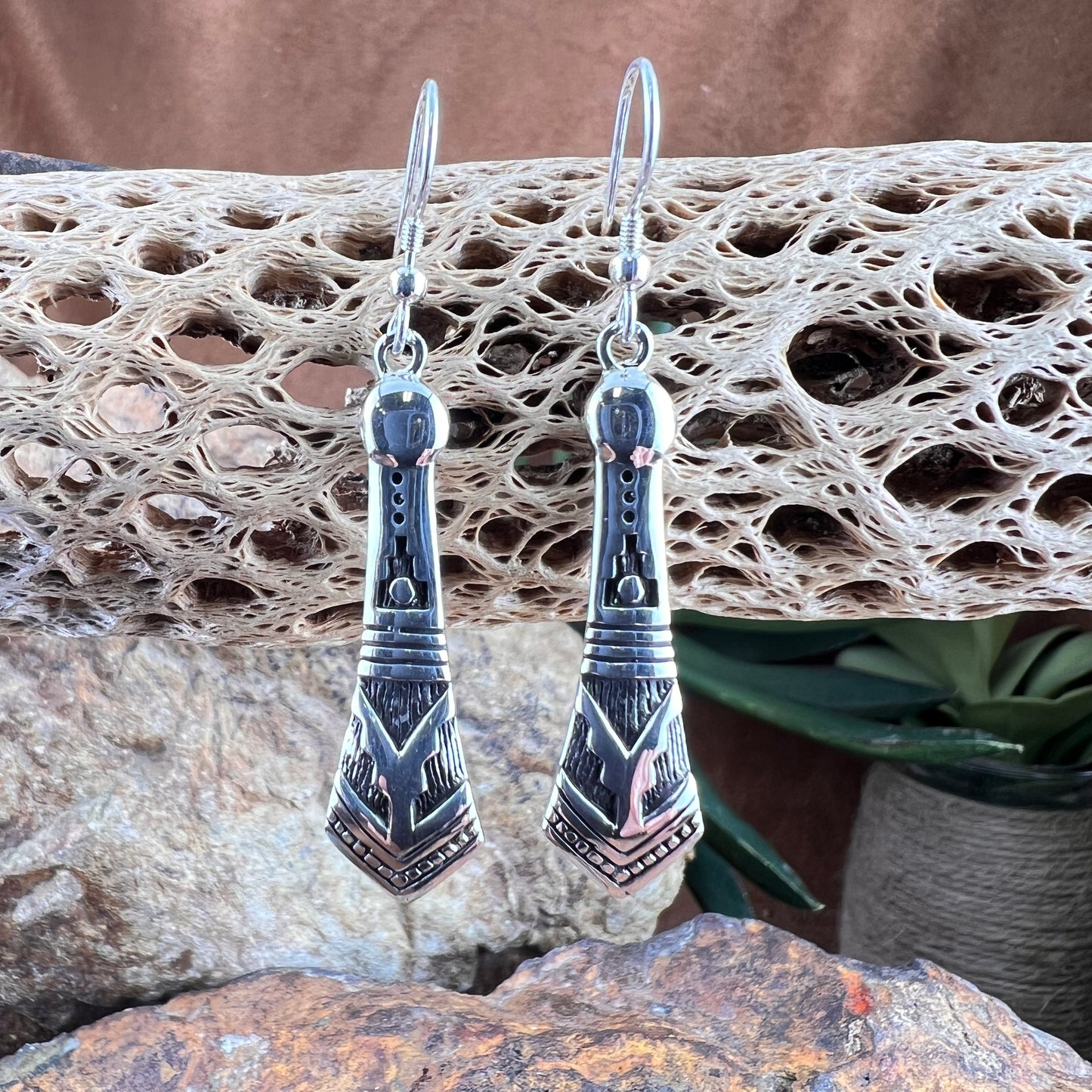 Silver earrings with geometric design on a textured stone surface