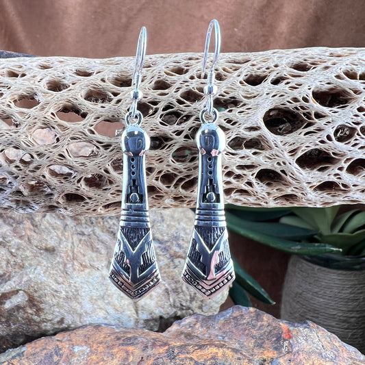 Silver earrings with geometric design on a textured stone surface