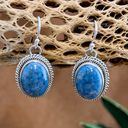 Angled view of sterling silver denim lapis dangle earrings with oval stones