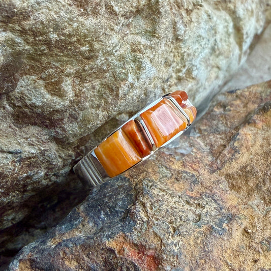 Spiny Oyster shell cobble inlay and sterling silver ring on a rock surface.
