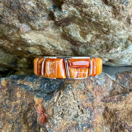 Spiny Oyster shell cobble inlay and sterling silver ring on a rock surface.