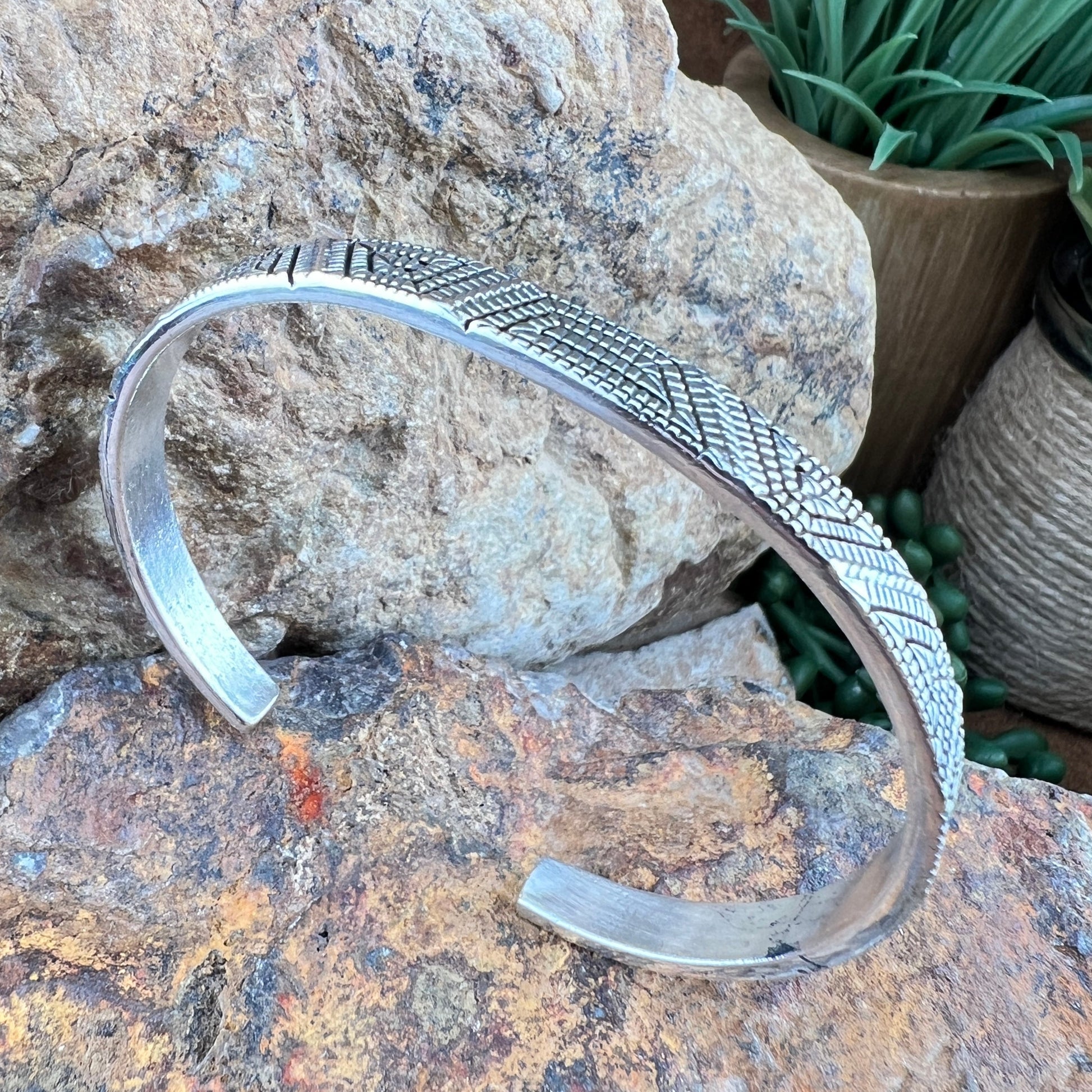 Silver bracelet with textured design on a rock surface