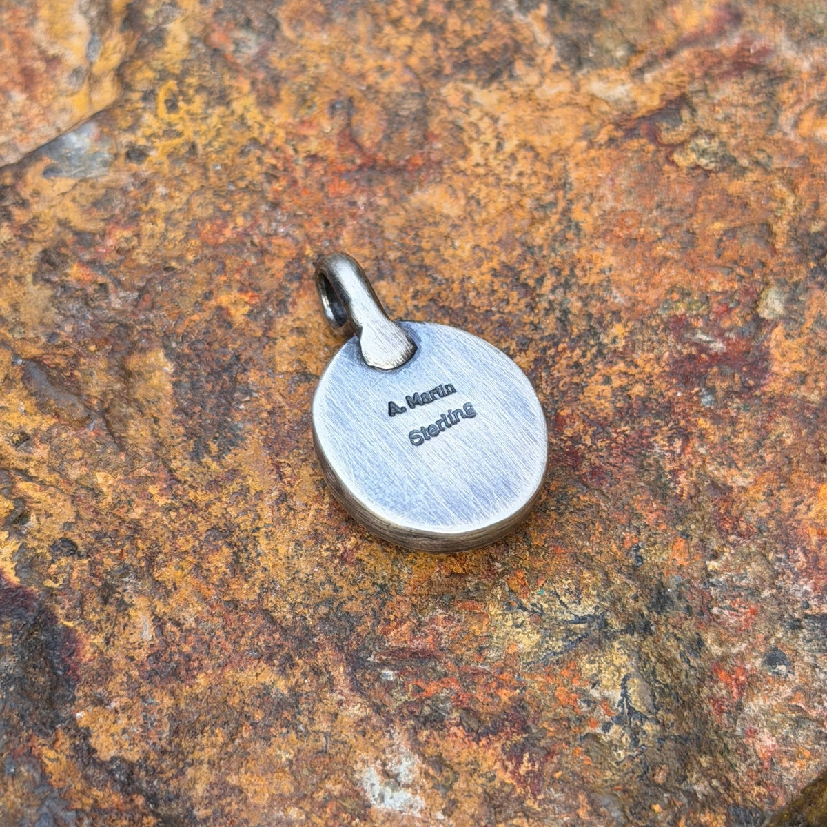 A light blue golden hills turquoise pendant with chocolate matrix by angela martin. this showcases the back of the pedant with stamping