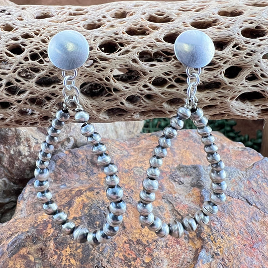 Silver hoop earrings with bead accents on a textured stone surface