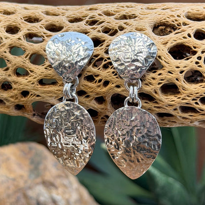 Hammer finished drop earrings by artie yellowhorse. They hang from a piece of driftwood