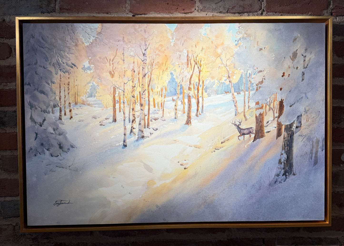 Framed winter landscape painting with a deer on a brick wall