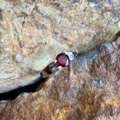 Silver ring with a red gemstone on a rocky surface