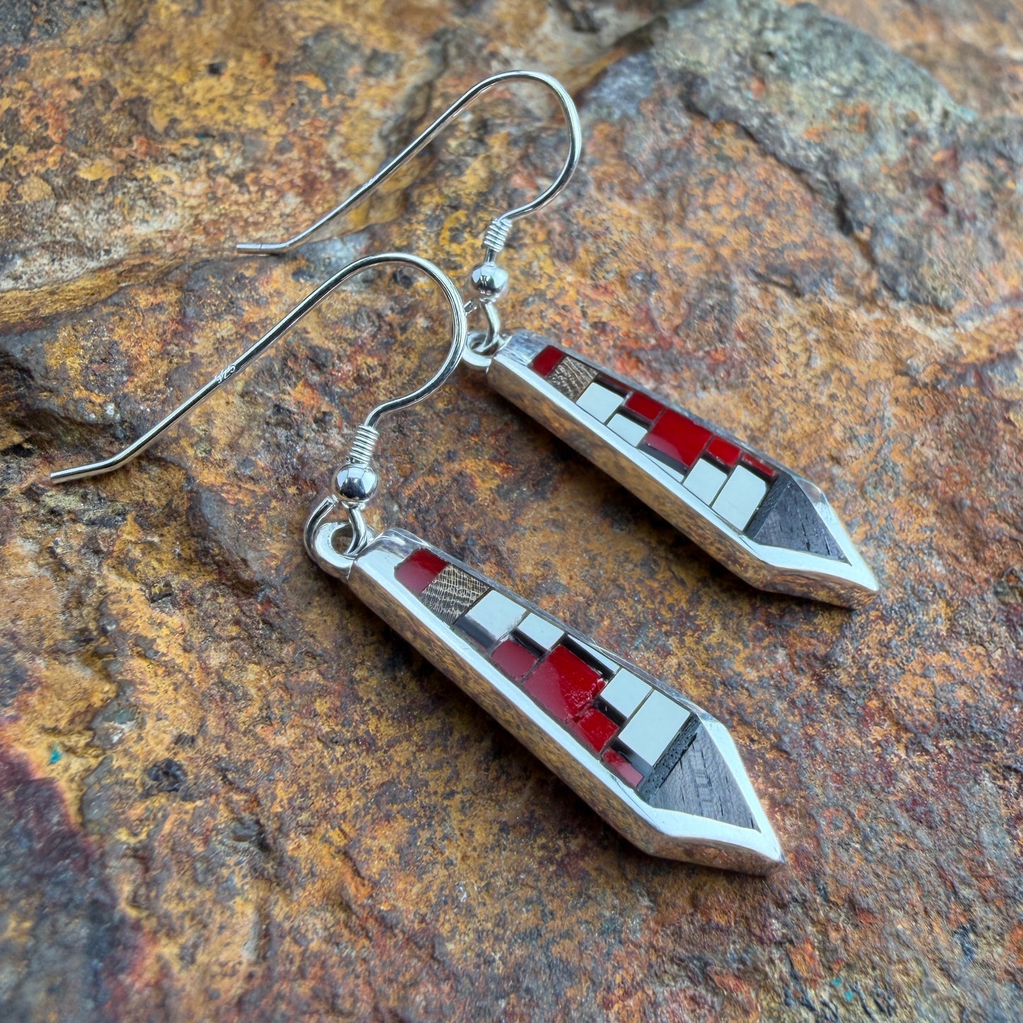 Pair of earrings with red and silver design on a stone surface