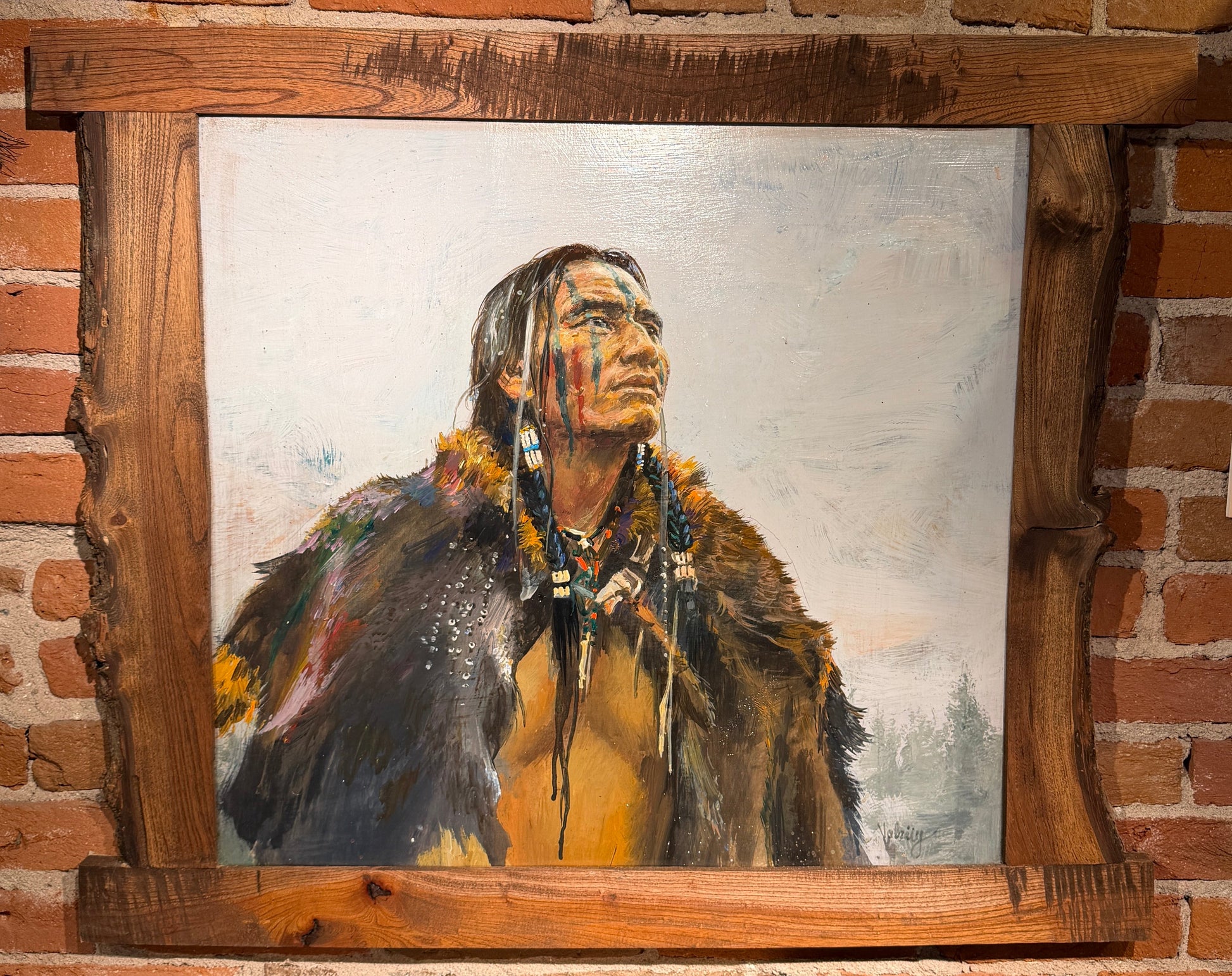 Painting of a Native American figure in a wooden frame against a brick wall.