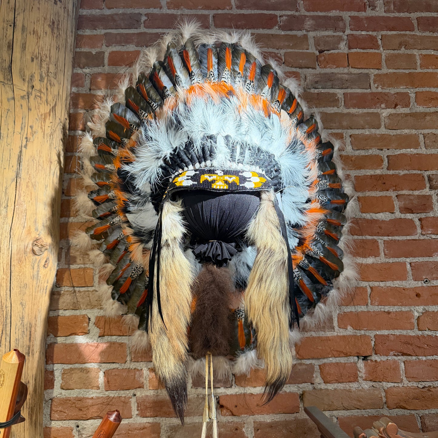 Feathered headdress with orange, black, and white colors on a brick wall background