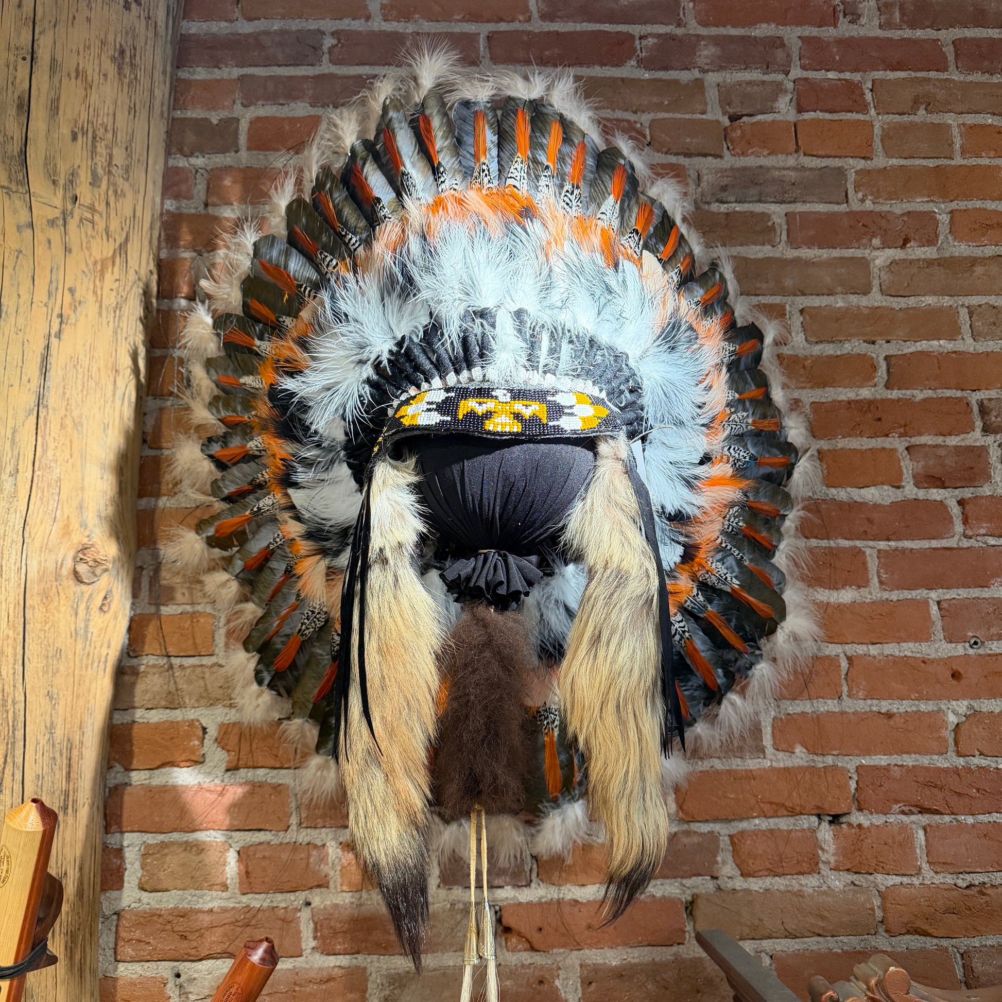 Feathered headdress with orange, black, and white colors on a brick wall background
