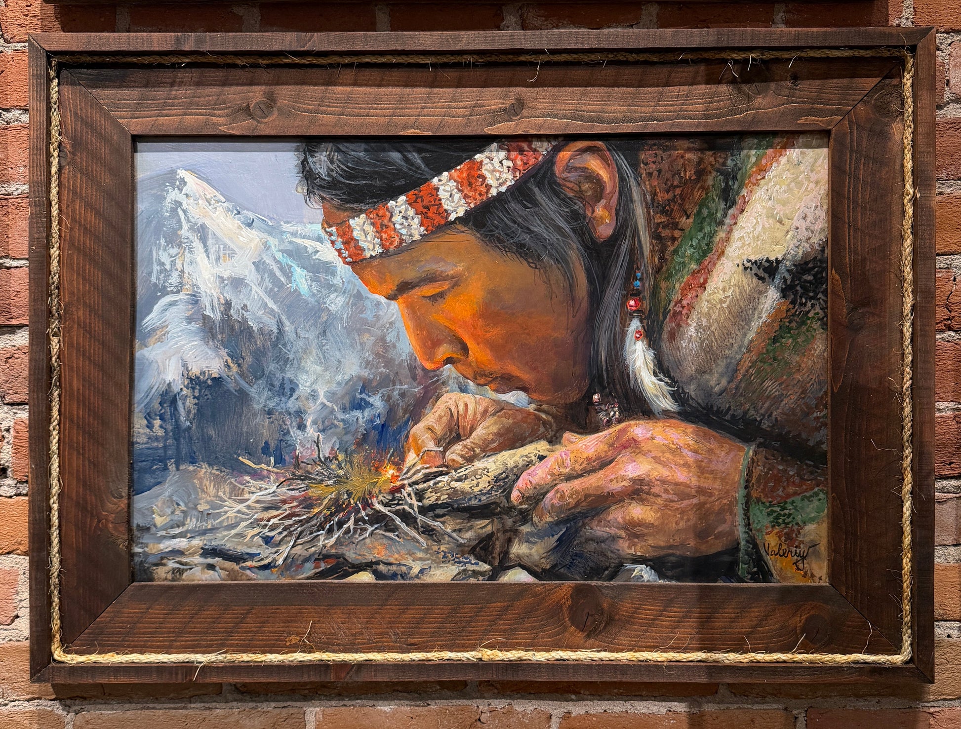Painting of a person preparing food with mountains in the background, framed and displayed on a brick wall.