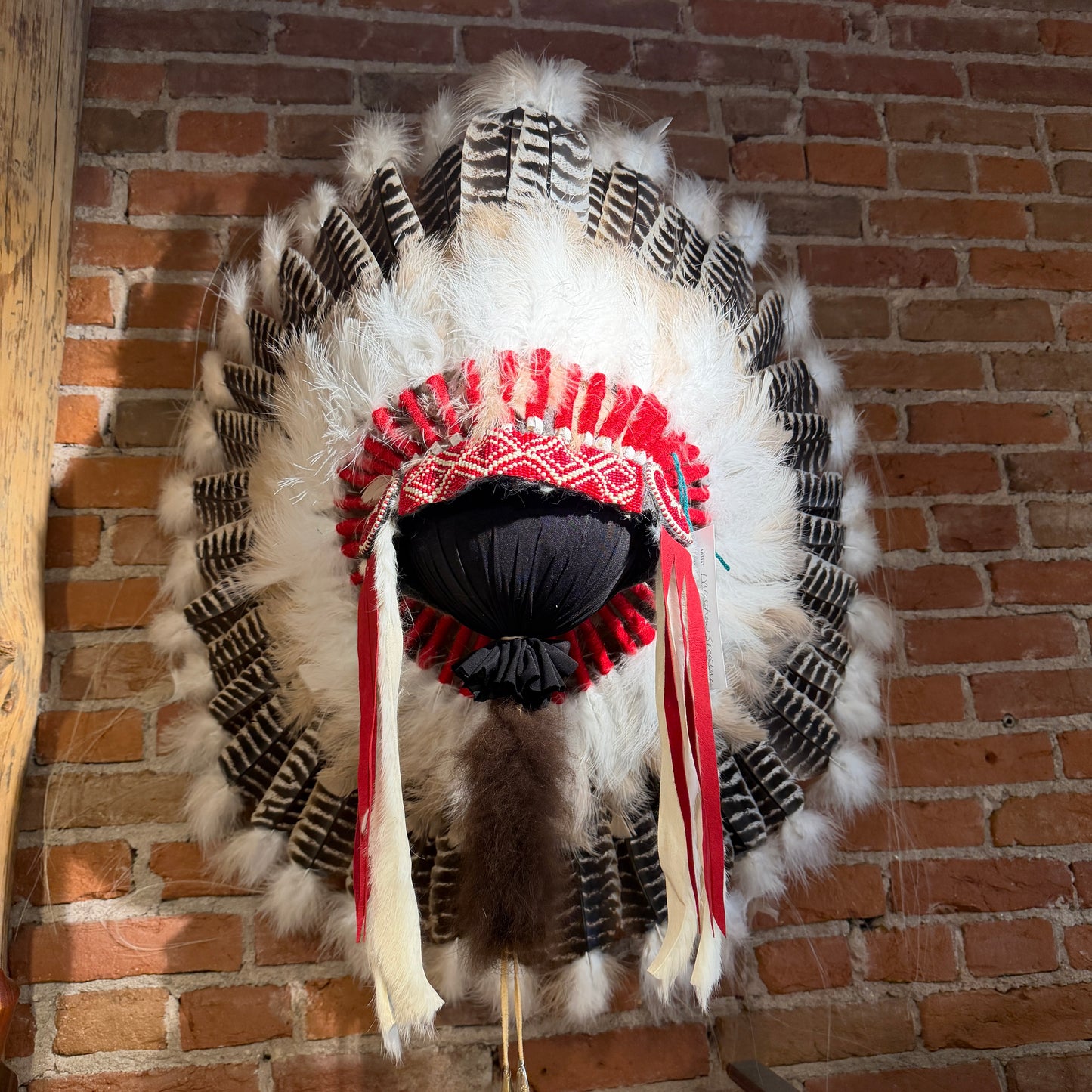 Feathered headdress with red and black accents against a brick wall