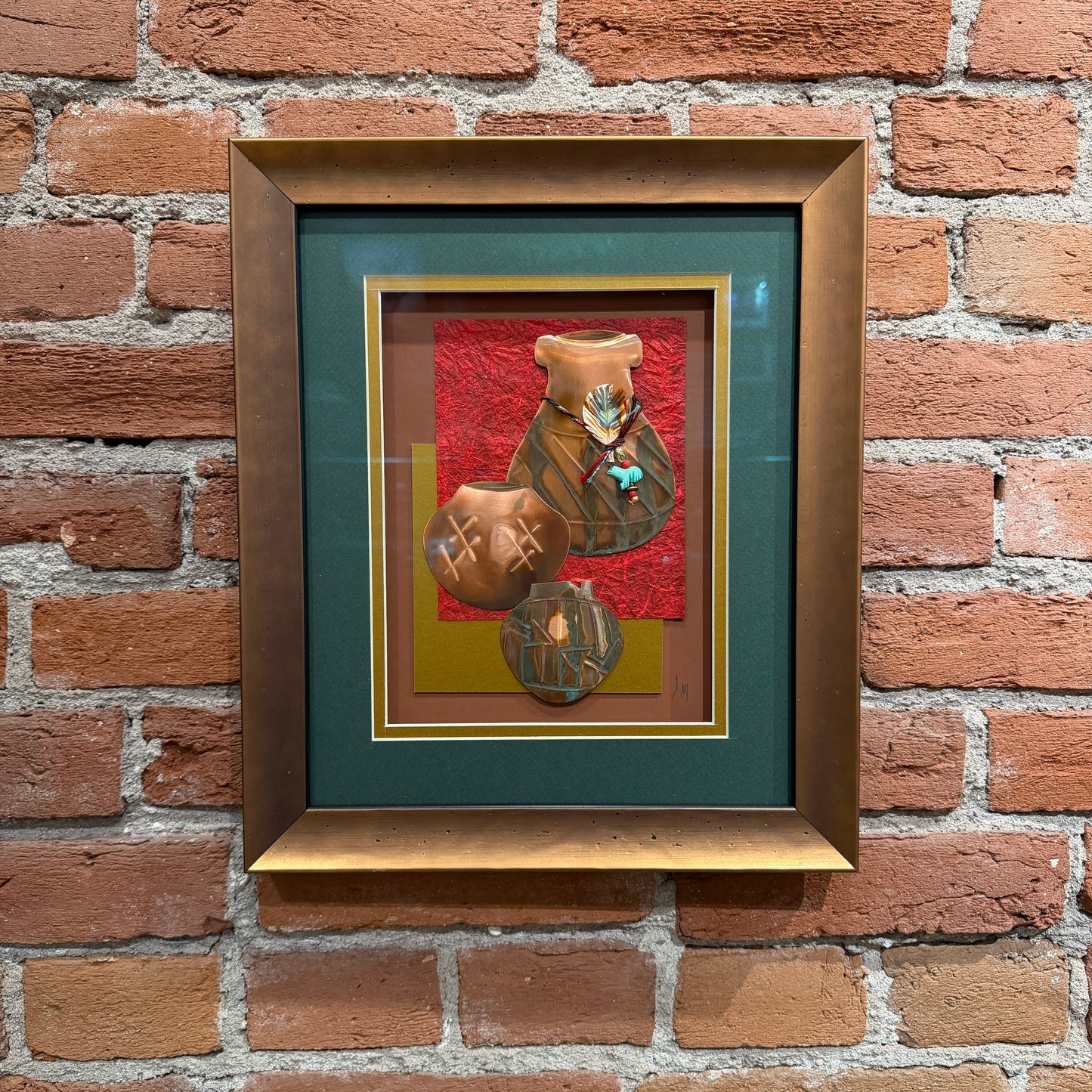 An art piece that contains thinly pressed copper shaped and detailed to represent three traditional Native American ceramic pots. They are placed in the foreground. The background is a dark teal, gold, and red. Framed in a copper-colored frame.