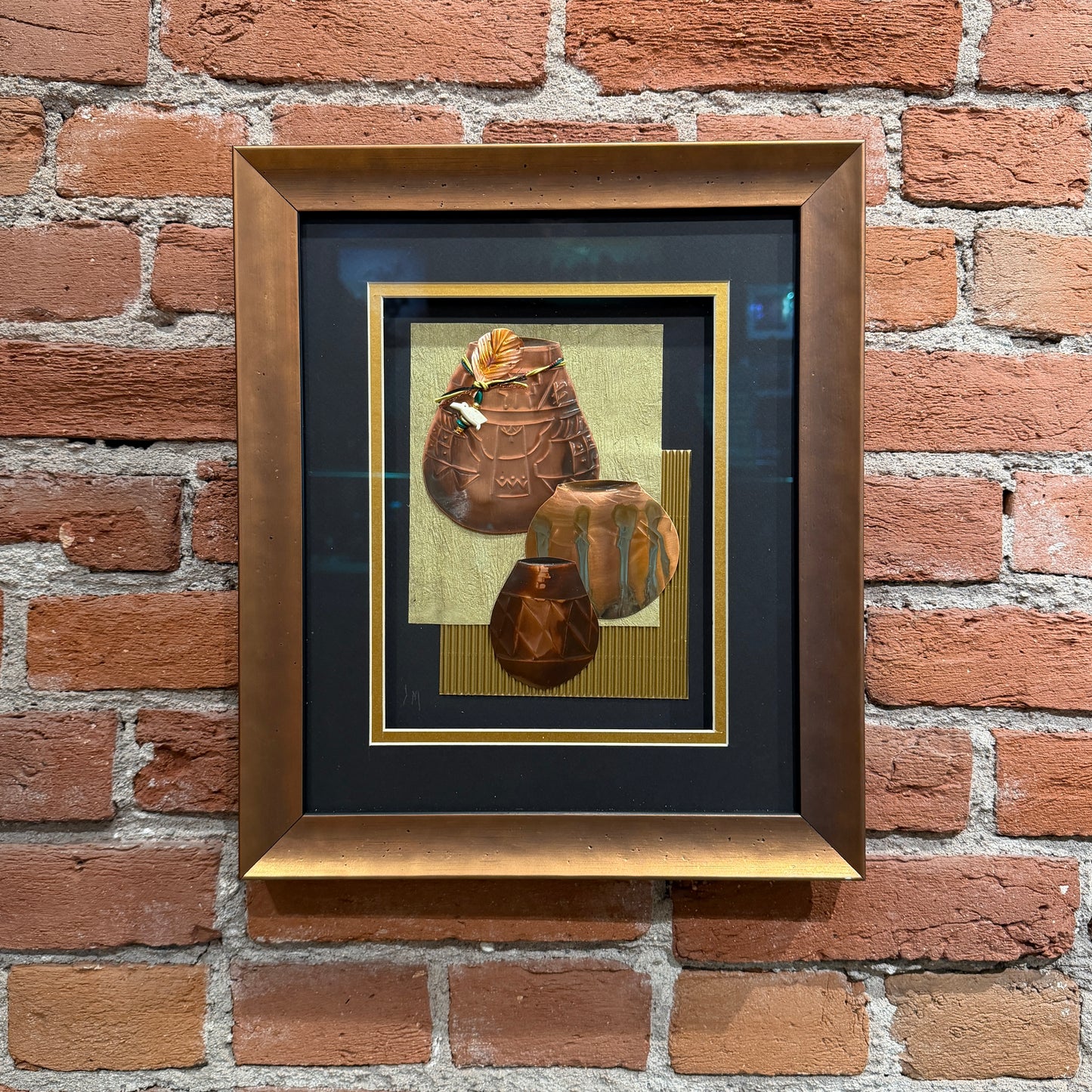 An art piece that contains thinly pressed copper shaped and detailed to represent three traditional Native American ceramic pots. They are placed in the foreground. The background is light green and gold. Framed in a copper-colored frame.