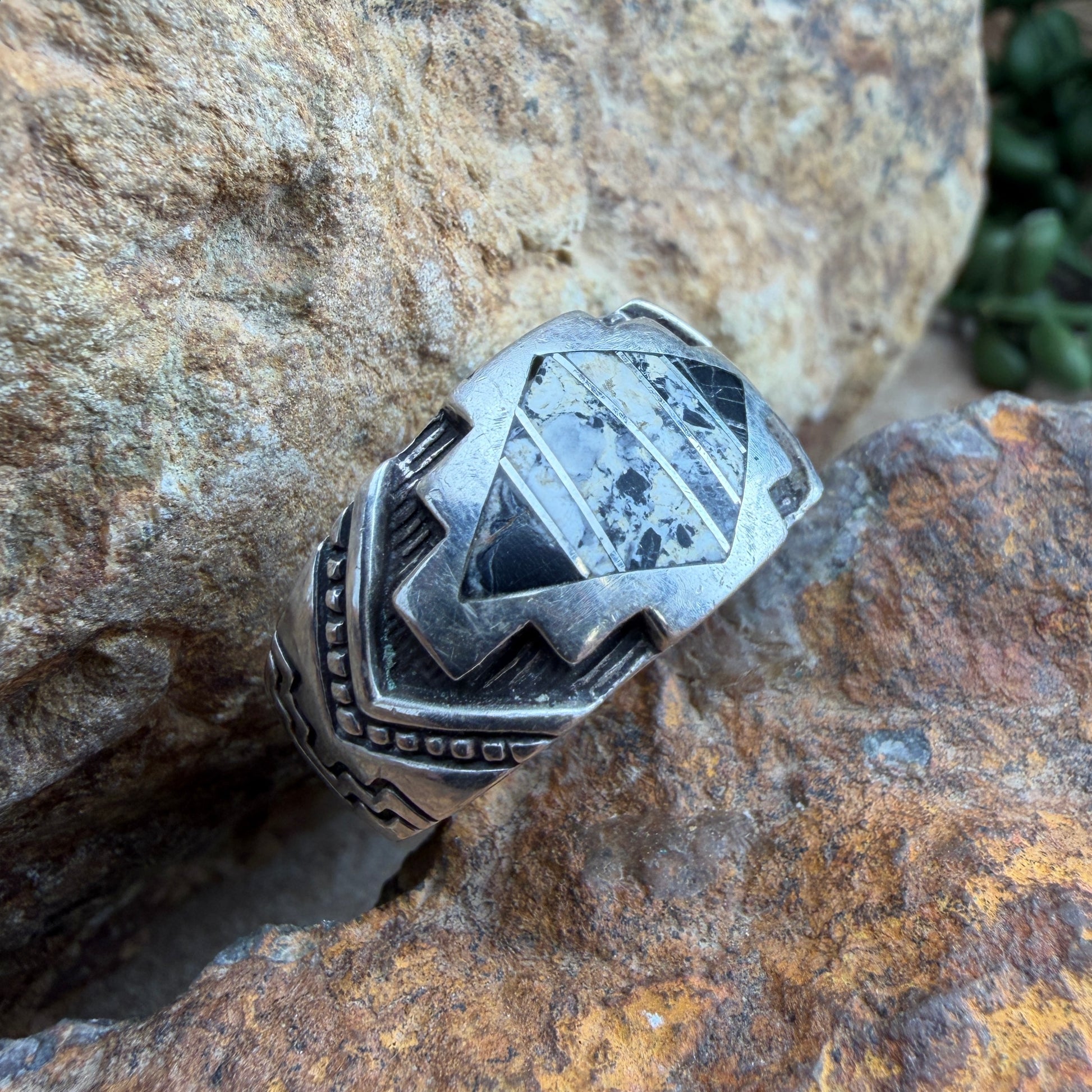 Silver ring with  white and black inlay set in geometric design that is then stamped around the band with further details.