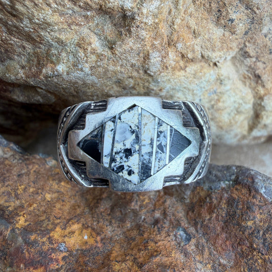 Silver ring with  white and black inlay set in geometric design that is then stamped around the band with further details.