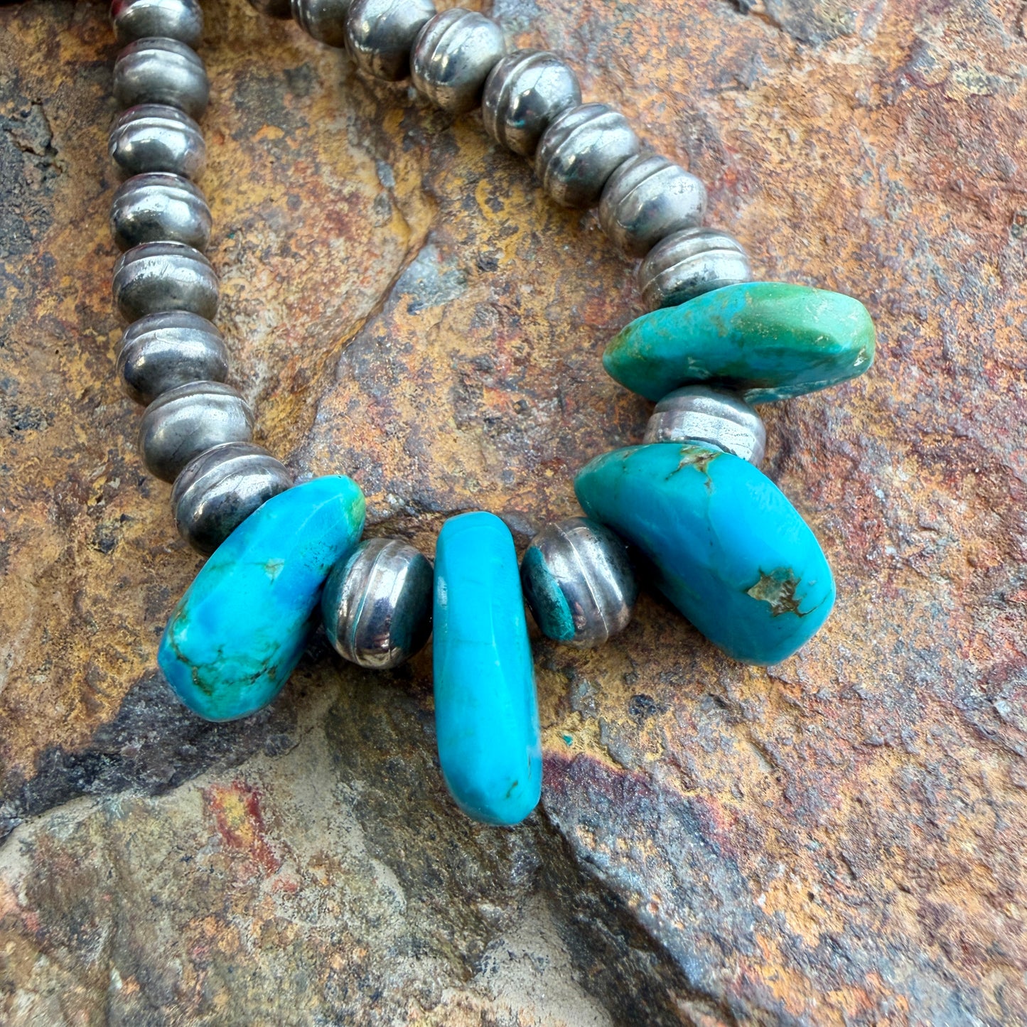 Necklace with turquoise beads and silver accents on a stone surface