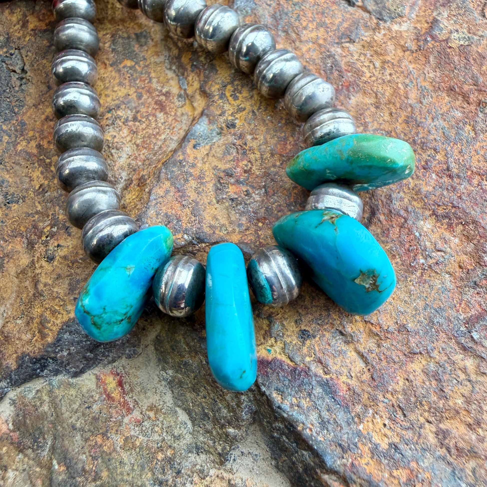 Necklace with turquoise beads and silver accents on a stone surface