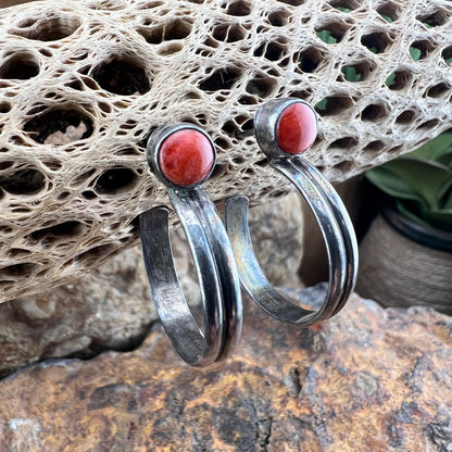Silver hoop earrings with orange stones on a textured stone surface