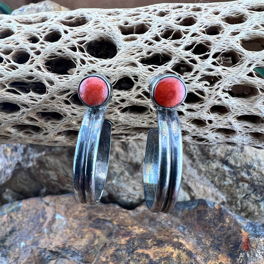 Silver hoop earrings with orange stones on a textured stone surface