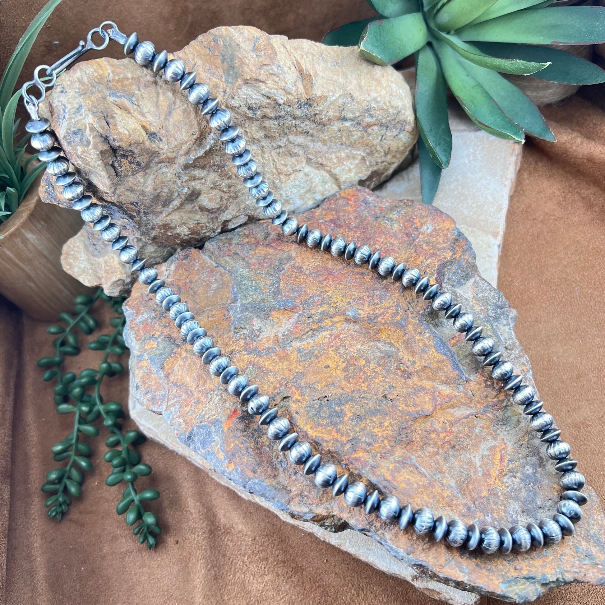 Silver beaded necklace on a textured stone surface with greenery